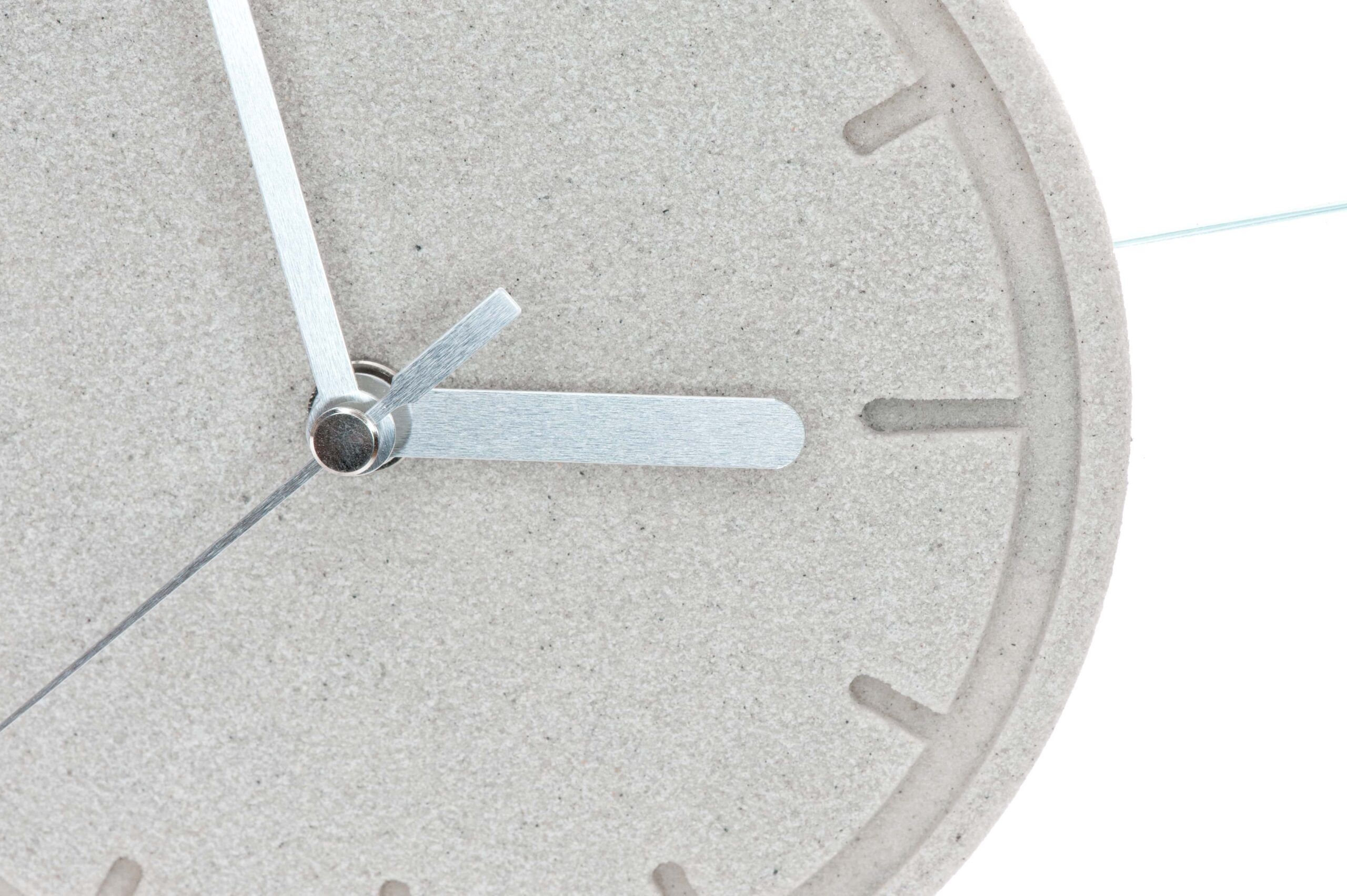 Nahaufnahme des Zifferblatts der Tischuhr „Susi“ aus Sandstein mit silbernen Minuten- und Stundenzeigern, die auf Viertel nach neun stehen.