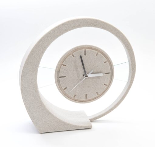 Eine moderne Tischuhr aus hellem Sandstein in Form einer geschwungenen Spirale, in deren Zentrum ein rundes Uhrwerk mit schlichten Strichmarkierungen und schwarzen Zeigern hinter Klarglas schwebt.